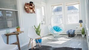 A bright room with a white chair, a hanging chair, and a wooden table with a plant.