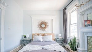 A bedroom with a bed, nightstands, a mirror, and a window with curtains.
