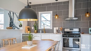 A modern kitchen with a wooden dining table, stainless steel appliances, and pendant lighting.