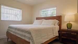 A bedroom with a wooden bed, two windows, a nightstand, and a lamp.