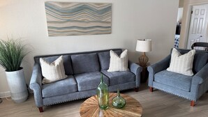 A living room with a grey sofa, two armchairs, a wooden coffee table, and a potted plant.