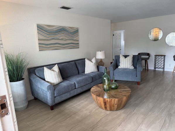 A living room with a grey sofa, a round wooden coffee table, and a potted plant.