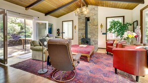 A spacious living room with a stone fireplace, leather sofas, and a large window overlooking a garden. - Lakefront Glen Ellen Cabin w/ Views Near Wineries! (Glen Ellen)