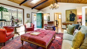 A spacious living room with a large red tufted sofa, a brown leather armchair, and a green door leading to another room. - Lakefront Glen Ellen Cabin w/ Views Near Wineries! (Glen Ellen)