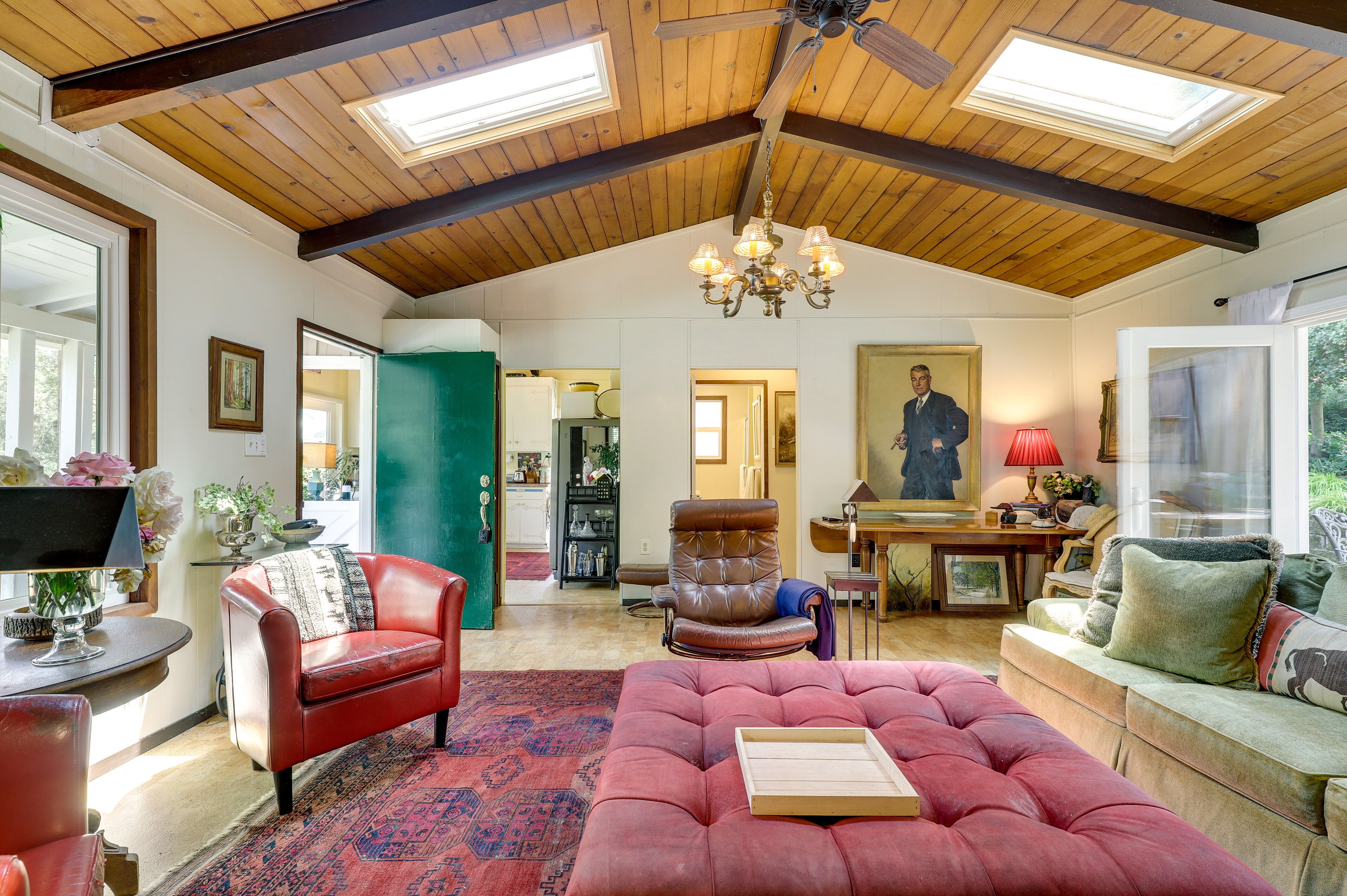 A spacious living room with a high ceiling, a chandelier, and a large window.