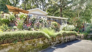 A house with a covered porch, surrounded by lush greenery and flowering plants. - Lakefront Glen Ellen Cabin w/ Views Near Wineries! (Glen Ellen)