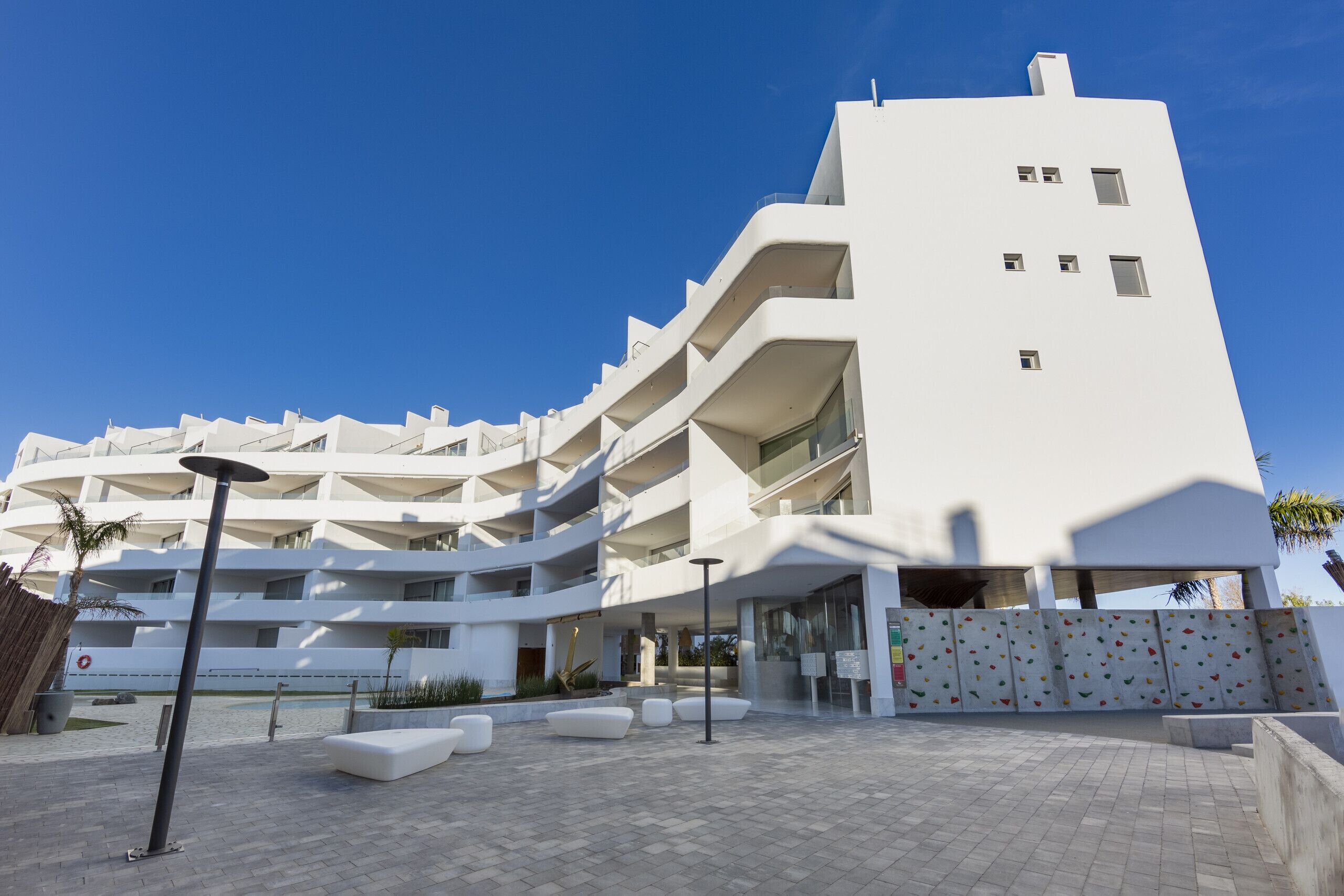 A modern multi-story building with a white facade, outdoor seating areas, and a clear blue sky.