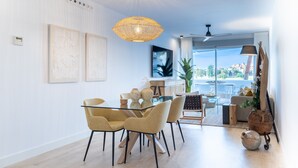 A modern dining area with a glass table and matching chairs, a large woven pendant light, and a view of the outdoors through a sliding glass door.