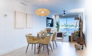 A modern dining area with a glass table and matching chairs, a large woven pendant light, and a view of the outdoors through a sliding glass door.