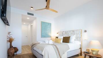 Een moderne slaapkamer met een groot bed, een plafondventilator, een schilderij aan de muur en een nachtkastje met een lamp.