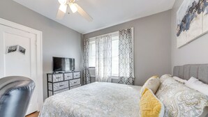 Une chambre à coucher comprenant un lit, une chaise, une commode, un téléviseur et un ventilateur de plafond.