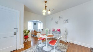 Un salon moderne avec une porte blanche, une table ronde accompagnée de deux chaises, un tapis moelleux et un luminaire suspendu au plafond.