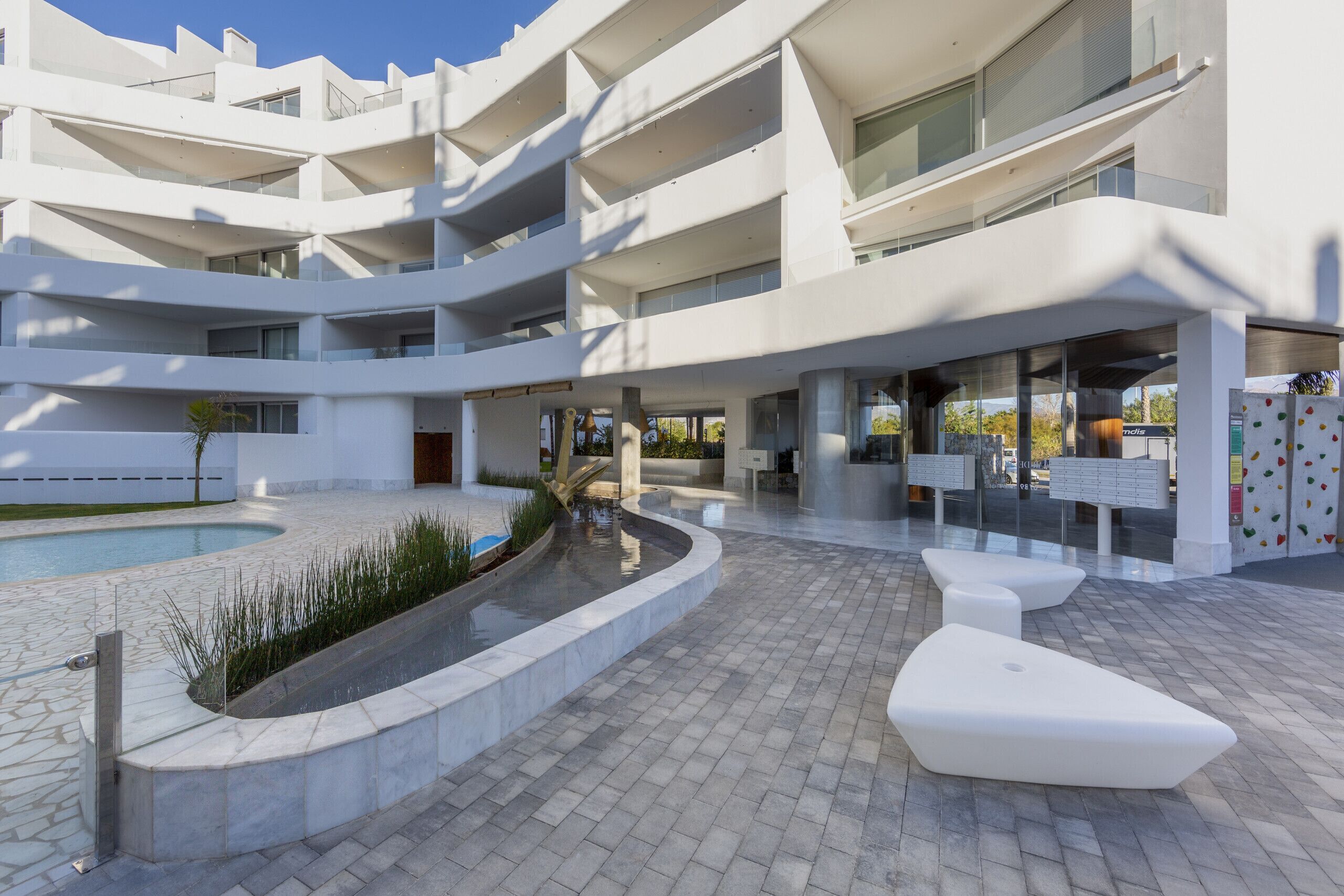 Un edificio moderno de varios pisos con piscina, zona de estar al aire libre y cielo despejado.