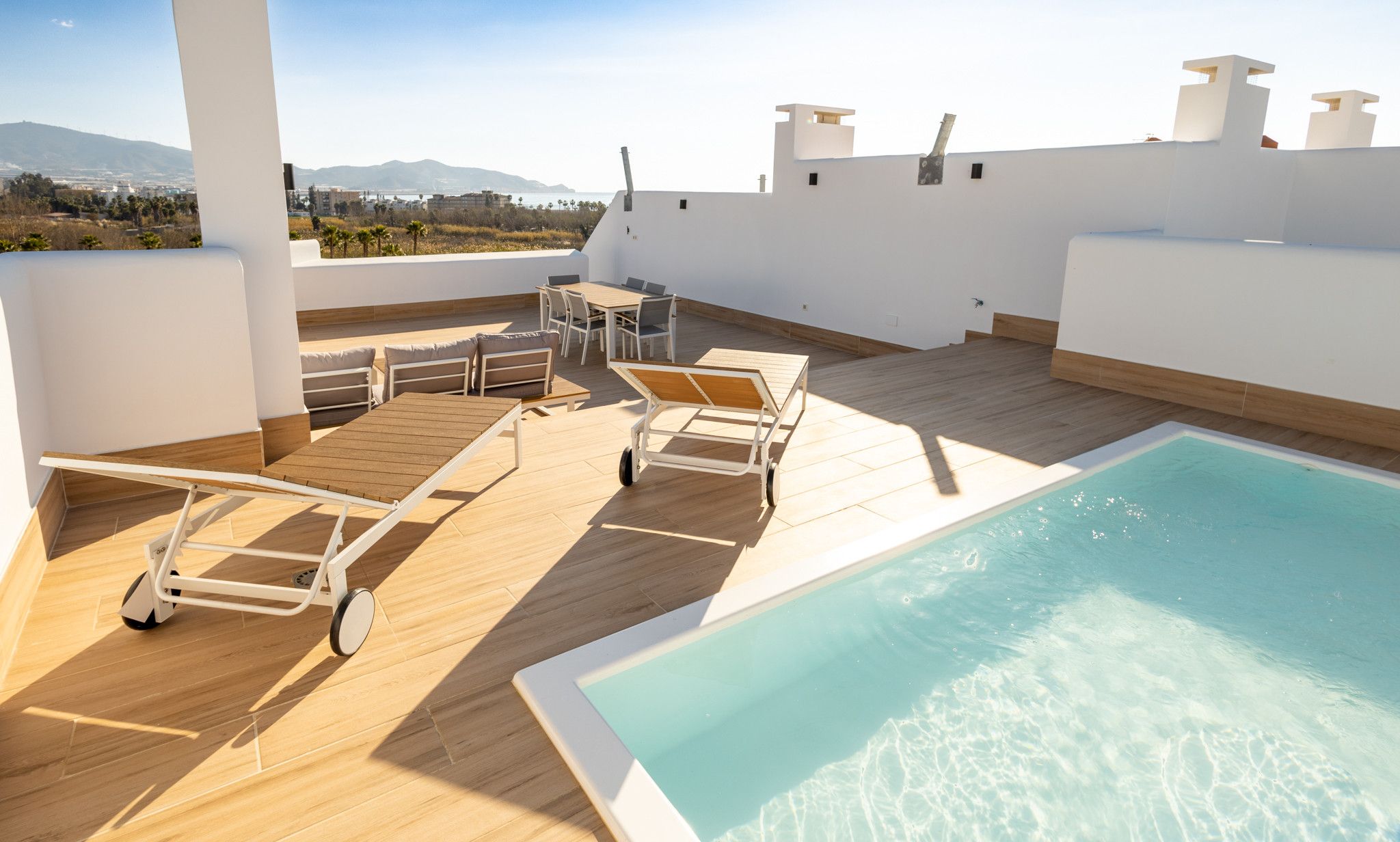Zona de piscina en la azotea con suelo de madera, sillas de descanso y vistas del paisaje.