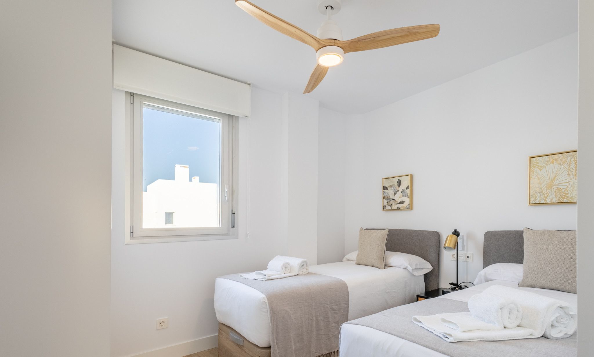 Een hotelkamer met twee bedden, een plafondventilator, een nachtkastje met lamp en kunstwerken aan de muren.