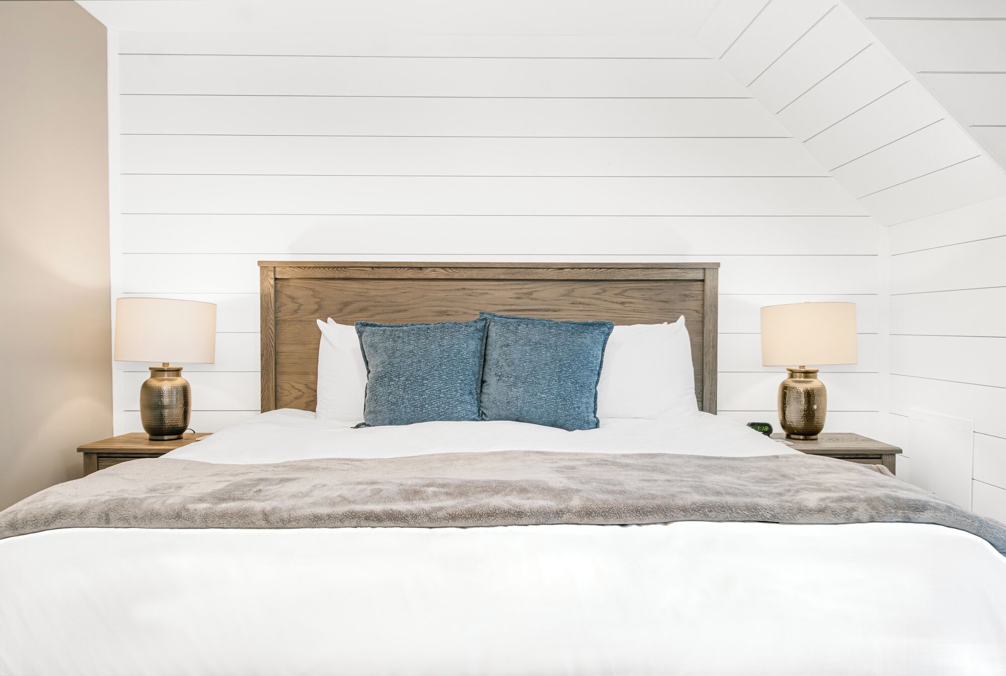 A bedroom with a wooden headboard, two bedside lamps, a bed with white bedding, and two blue pillows.