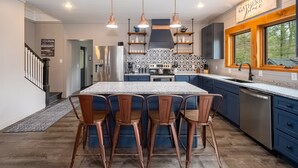 A modern kitchen with a central island, bar stools, pendant lighting, and a backsplash with a geometric pattern. - Gathering Place: Lakefront w. boat slip | Dog friendly | Hot tub | Fire pit (Oakland)