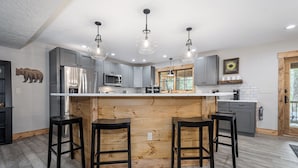 Una cocina moderna con una isla central, taburetes de bar, electrodomésticos de acero inoxidable e iluminación colgante.