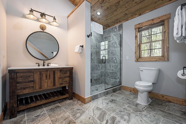 Un baño con tocador de madera, cabina de ducha de vidrio y un inodoro.