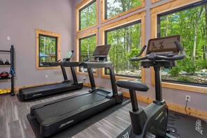 A gym with treadmills, a laptop on one, and large windows with a forest view.