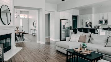 A modern living room with a fireplace, a sofa, and a coffee table. There is a kitchen area with white cabinets and stainless steel appliances.