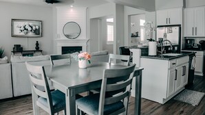A modern kitchen with white cabinetry, a dining area with a table and chairs, and a fireplace.