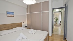 A bedroom with a bed, white towels, a nightstand, a lamp, a painting, and a wardrobe.