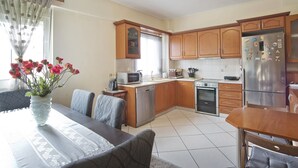 A modern kitchen with wooden cabinets, a stainless steel refrigerator, and a dining area with a table and chairs. - Paradeisos Modern, 2BR, 2BA, Fully Equipped (Chalandri)