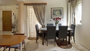 A dining area with a wooden table and six chairs, a vase with flowers, and a painting on the wall. - Paradeisos Modern, 2BR, 2BA, Fully Equipped (Chalandri)