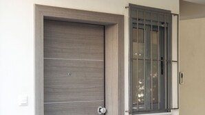 Eine moderne Tür mit strukturierter Oberfläche und einem runden Griff, neben einem Fenster mit Metallgitter.