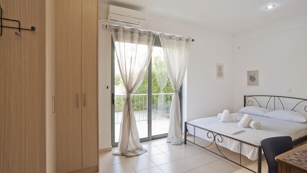 Ein Schlafzimmer mit einem Bett, einem Sessel, einem Schreibtisch und einem Fenster mit Vorhängen.