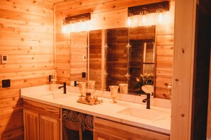 A wooden cabin-style bathroom with a large mirror, two sinks, and a vanity area. - Woodland Bluff (Port Angeles)
