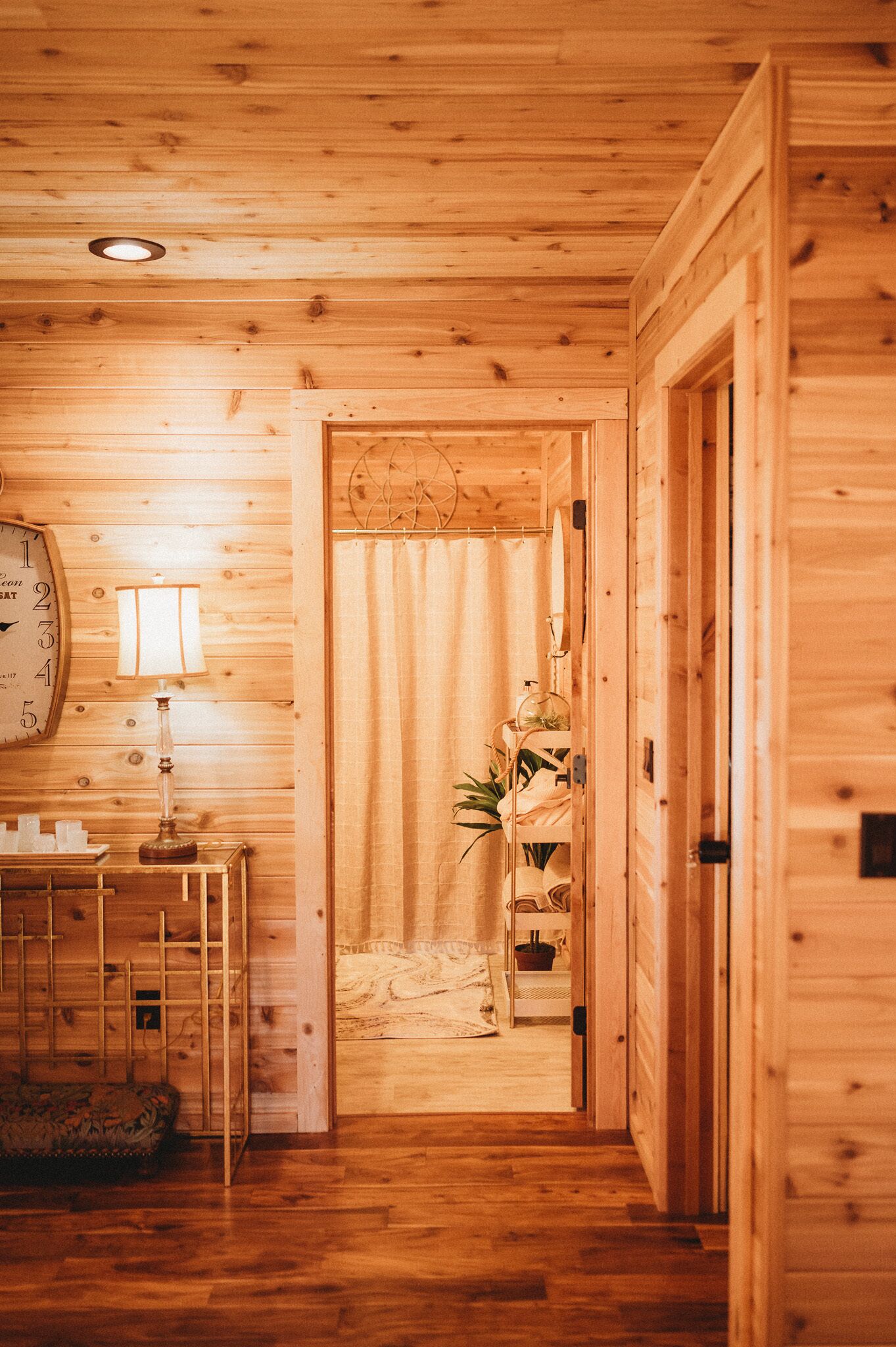 A wooden interior hallway with a clock, a lamp, and a plant.