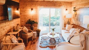 A cozy wooden cabin interior with a sofa, chairs, a coffee table, and a large window. - Woodland Bluff (Port Angeles)
