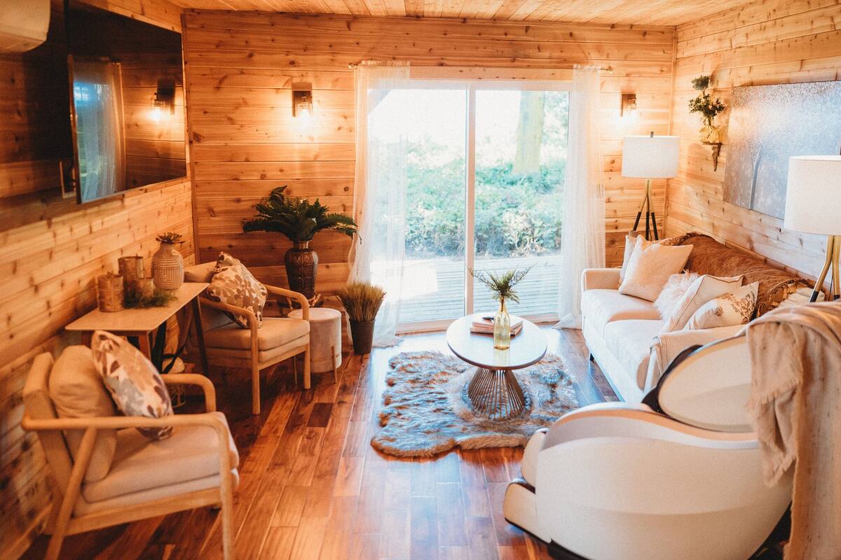 Ein gemütliches Holzhaus-Interieur mit einer Couch, Sesseln, einem Couchtisch und einem großen Fenster.