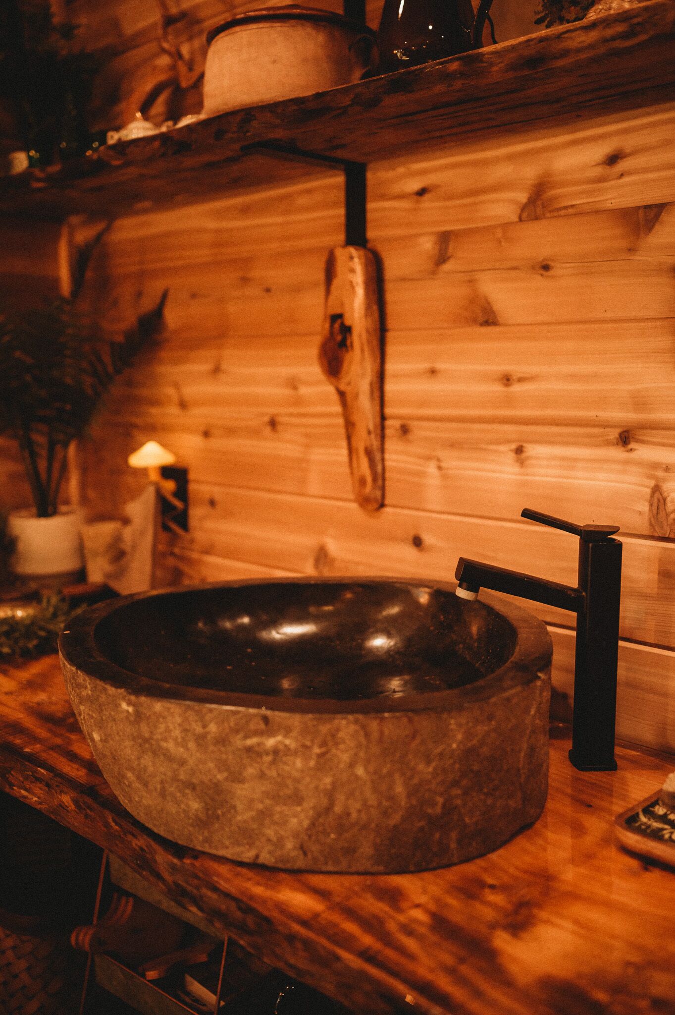 A rustic wooden interior with a large stone sink and a wooden shelf above it.