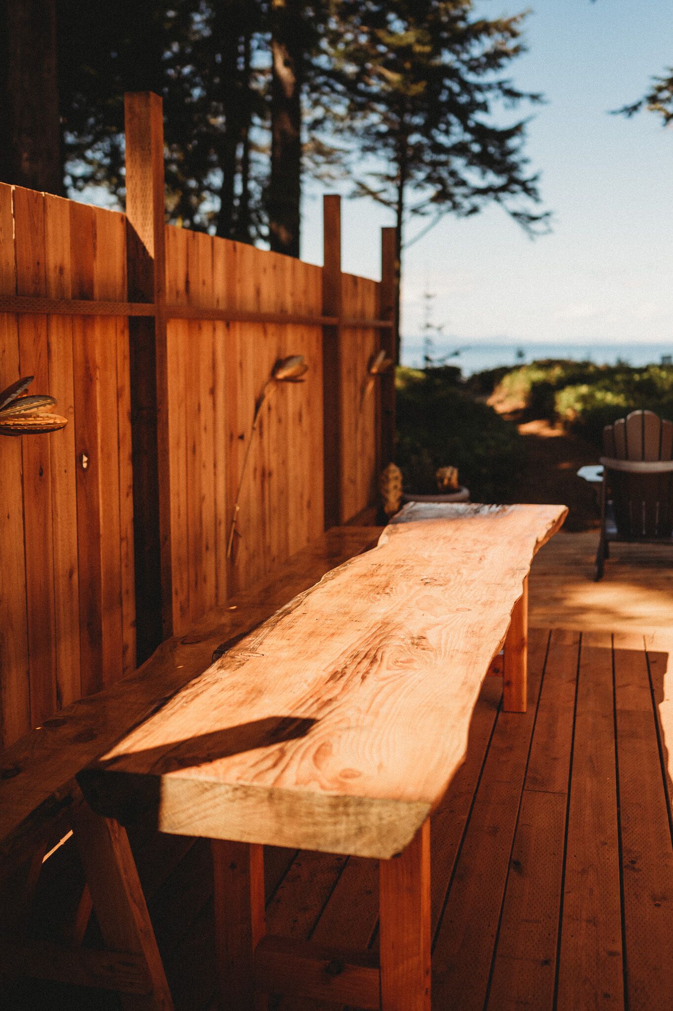Une terrasse en bois avec un banc et des chaises, entourée d’une clôture en bois et d’arbres.