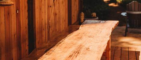 Une terrasse en bois avec un banc et des chaises, entourée d’une clôture en bois et d’arbres.