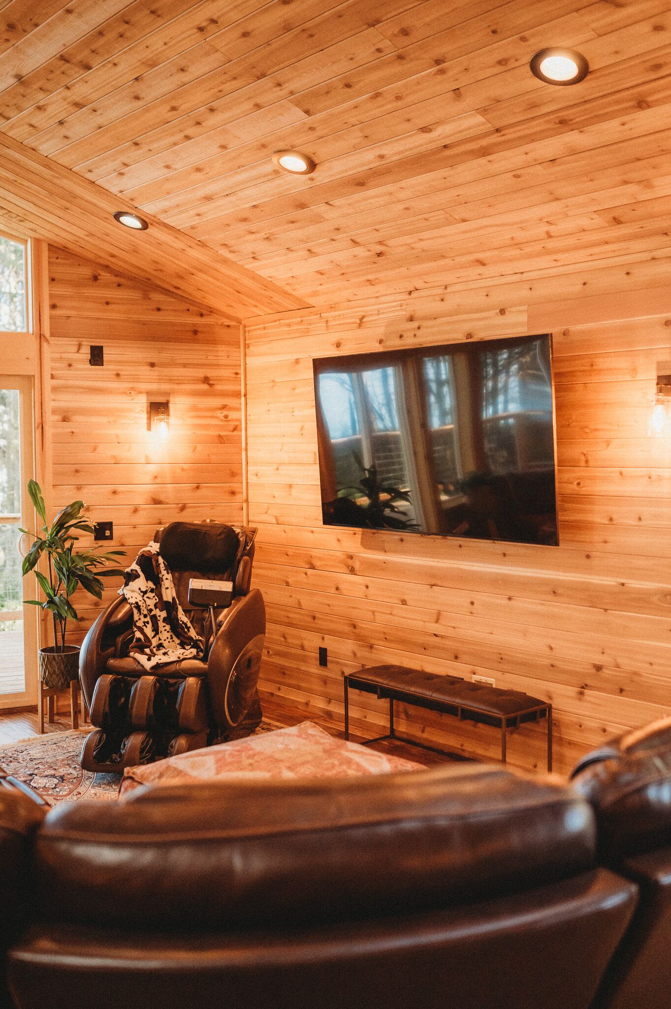 Un intérieur en bois comprenant un fauteuil de massage, un téléviseur à écran plat et un banc.