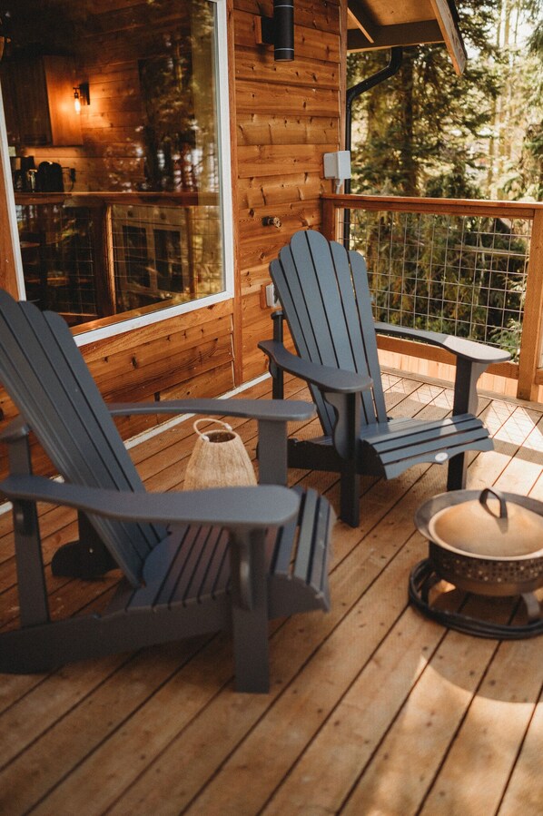 A wooden deck with two Adirondack chairs and a small table, overlooking a forested area. - Woodland Bluff (Port Angeles)