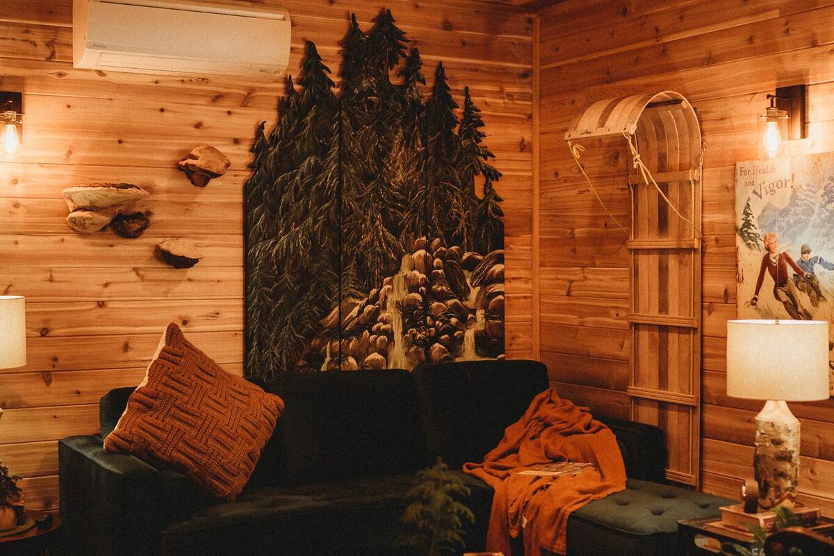 Ein gemütliches Blockhaus-Interieur mit Holzwänden, einer großen Baum-Wandmalerei, einem Sofa, einem Couchtisch und einer Lampe.