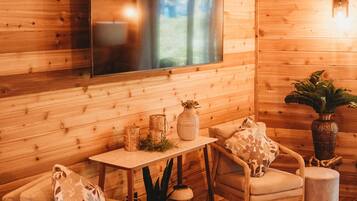 Ein gemütlicher Holzraum mit einem großen Flachbildfernseher, zwei Sessel, einem kleinen Tisch mit Dekoration und einer Zimmerpflanze.