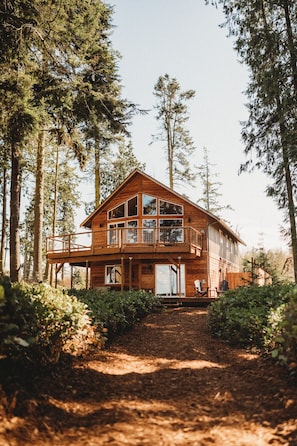 A wooden cabin with a balcony, surrounded by tall trees. - Woodland Bluff (Port Angeles)