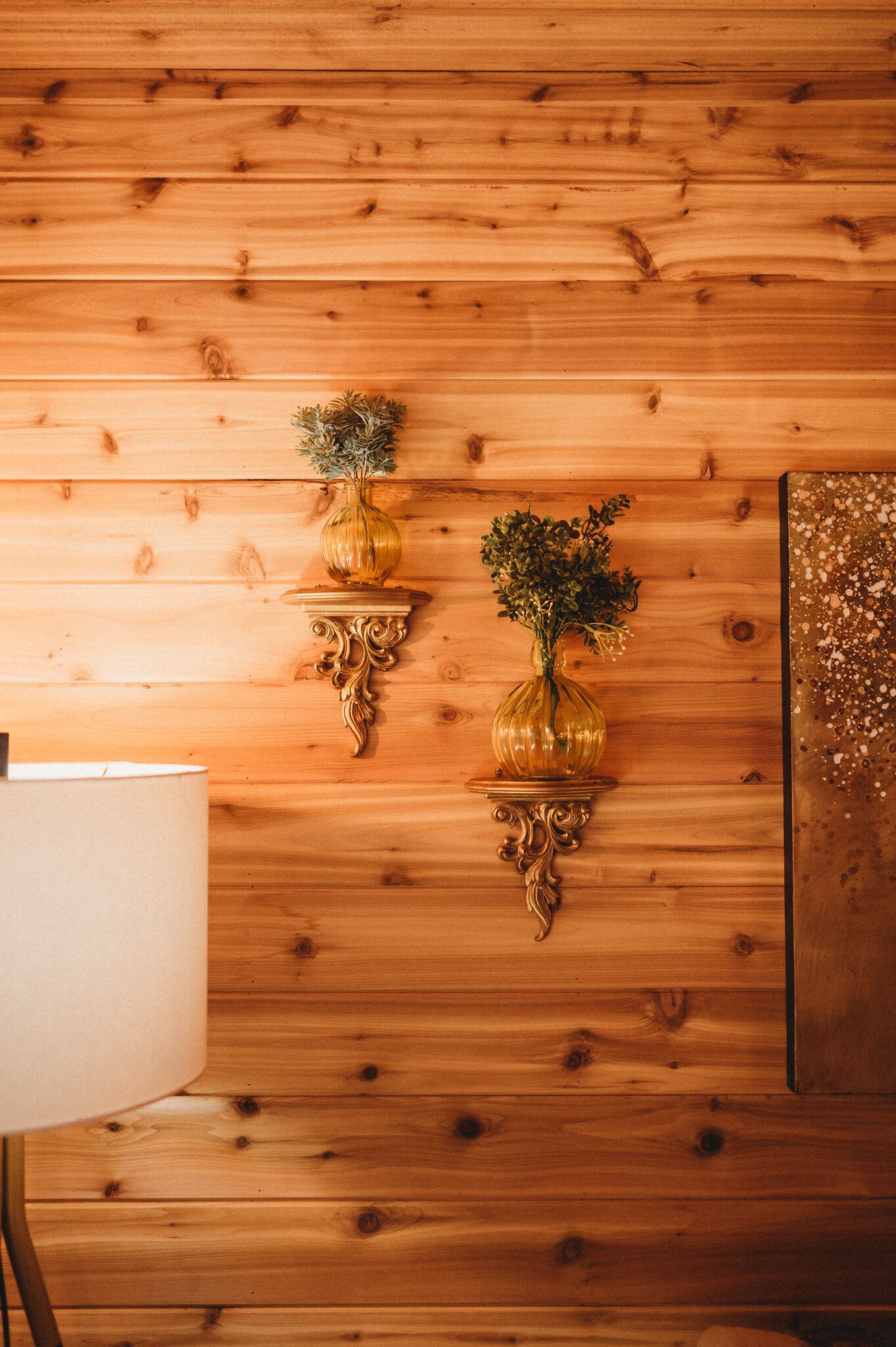 A wooden wall with two ornate gold vases on wall-mounted shelves.