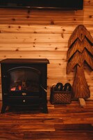 A wood-burning stove with a basket of slippers beside it, set against a wooden wall.