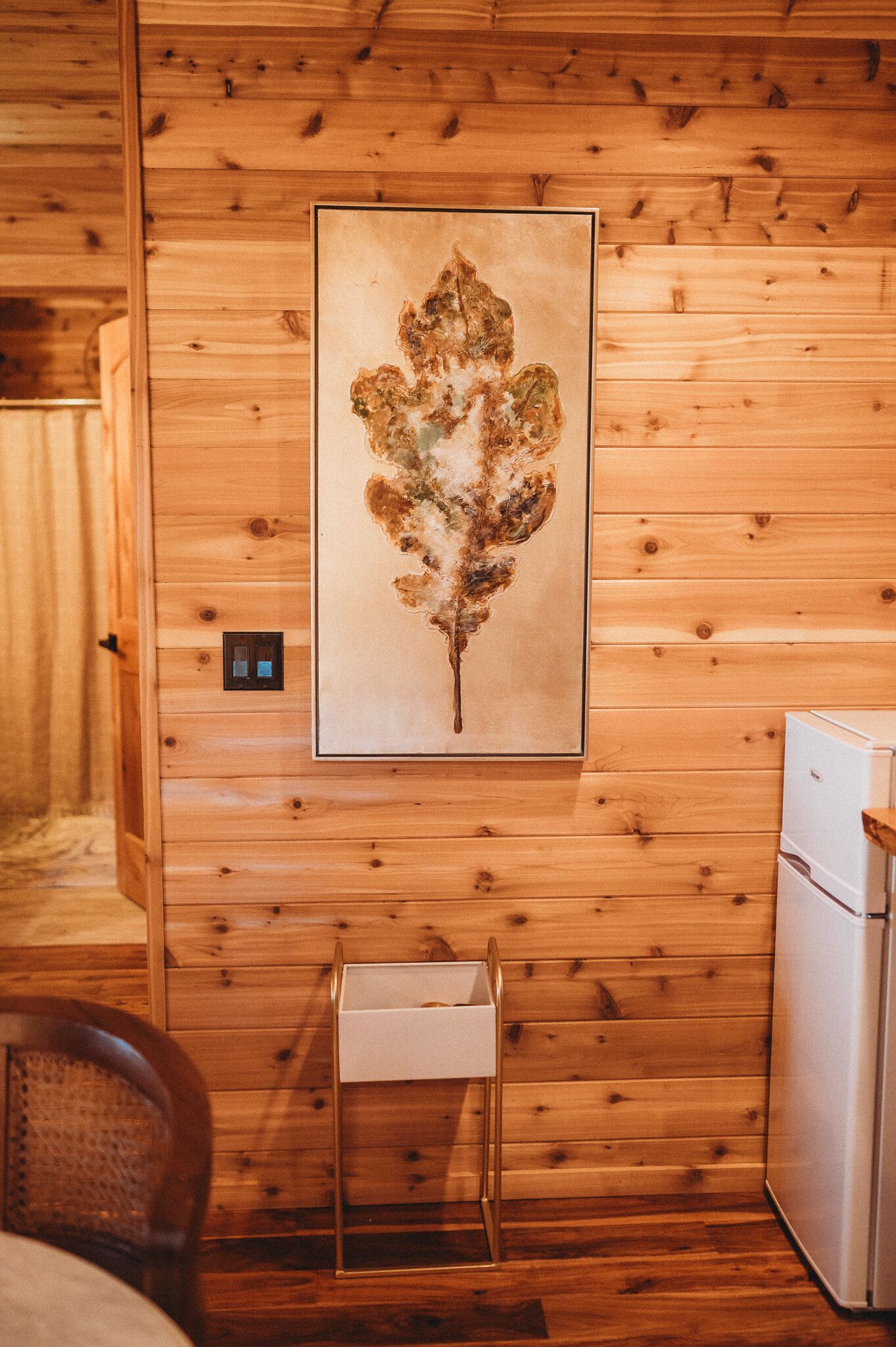 L’intérieur d’une cabane en bois, avec une œuvre d’art encadrée accrochée au mur, une petite table et un réfrigérateur.