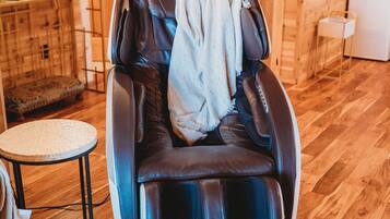 A massage chair in a wooden cabin room with a small round table and a lamp.