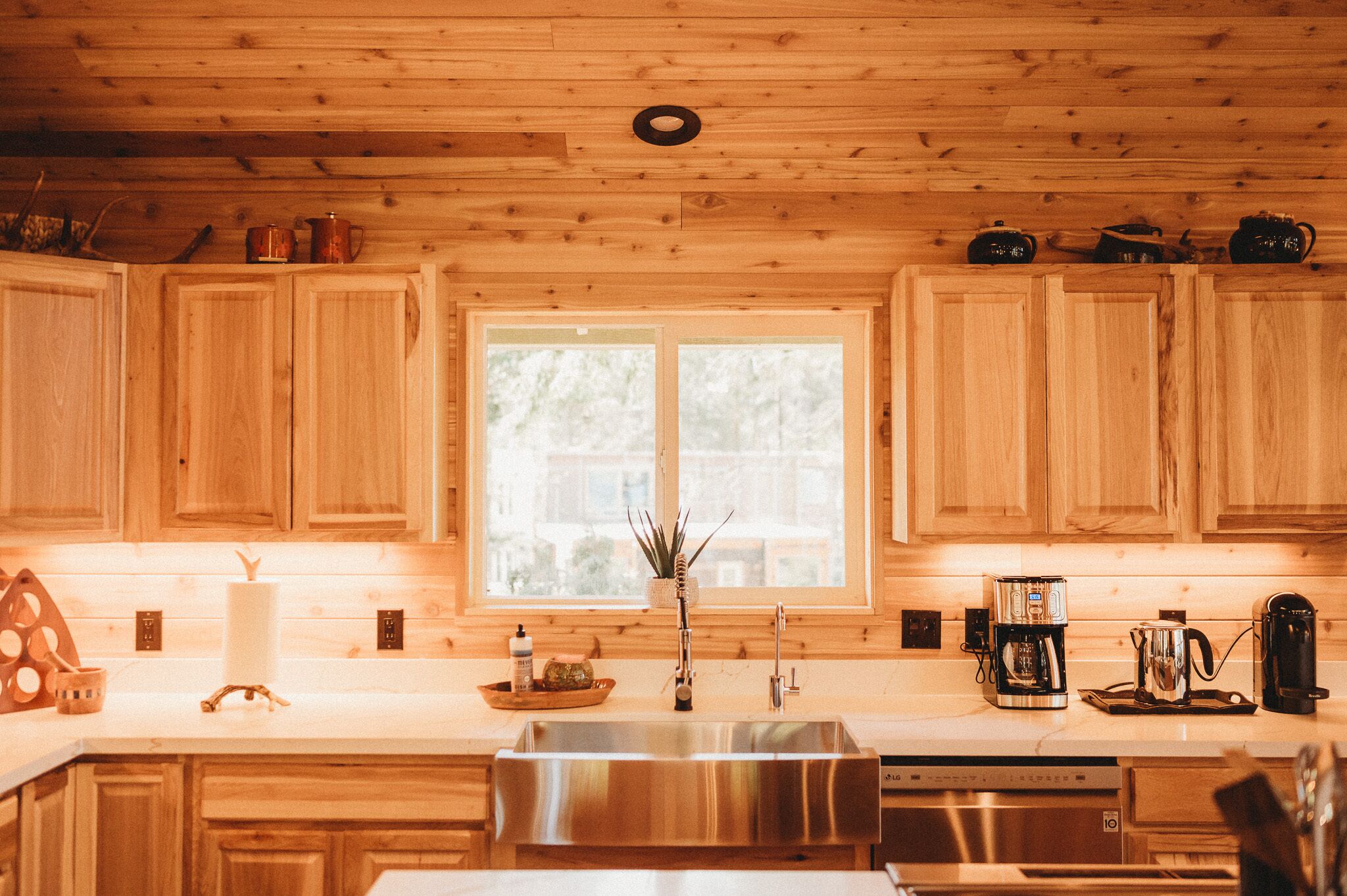 A kitchen with wooden cabinets, a stainless steel sink, and a window with a view of trees.