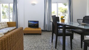 A modern living room with a sofa, a TV on a stand, a dining table with chairs, and a window with curtains.
