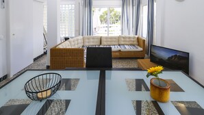 A modern living room with a sofa, a TV, and a glass coffee table with a flower vase.